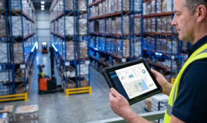 Supervisor en un centro de distribución logística utilizando una tableta industrial para monitorear datos en tiempo real gracias a la migración a la nube Azure para empresas.